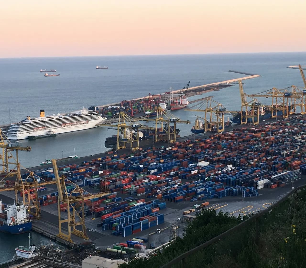 A container port with cranes and stacked shipping containers at dusk